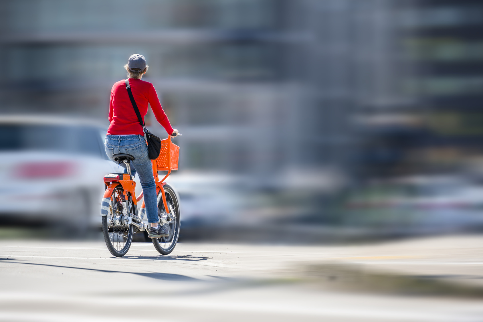 Woman on an orange bike with basket rides on bike path on the road next to other vehicles