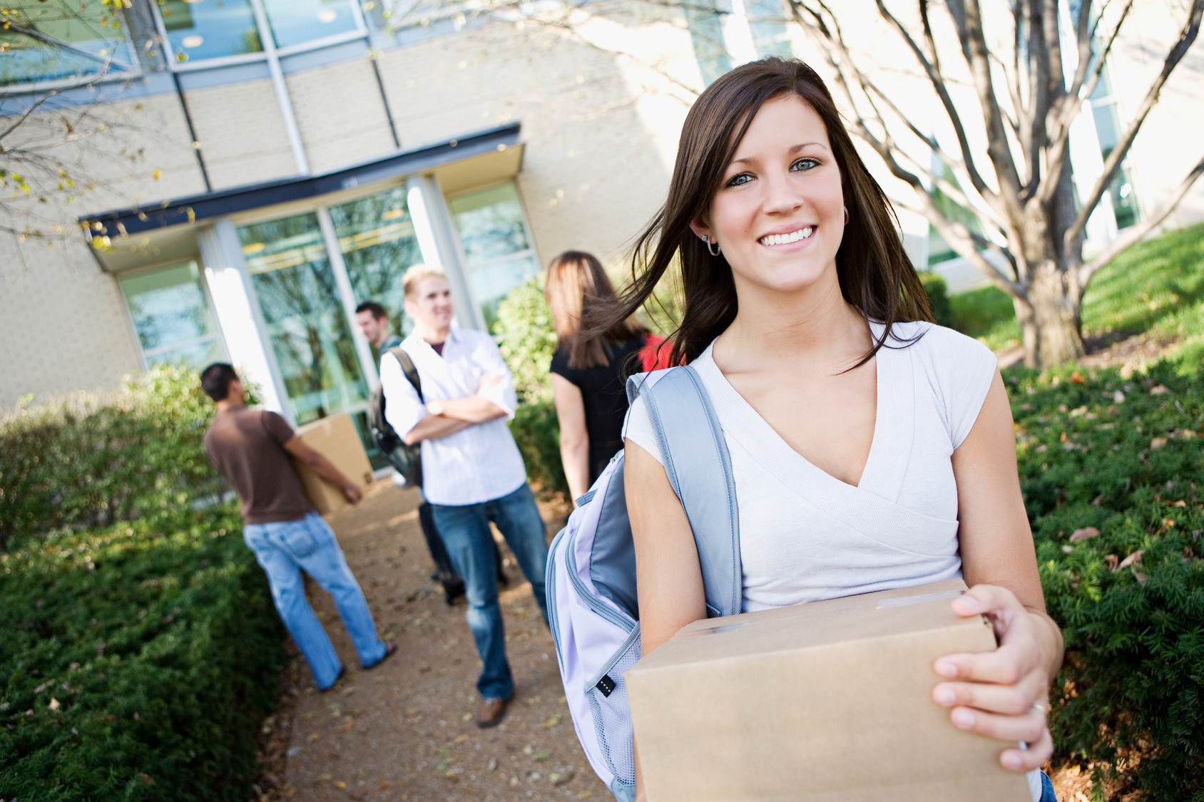 College-Girl-Smiling-Holding-Box-Walking-Outside