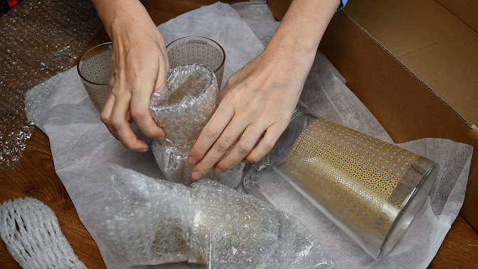 Woman hands pack up breakable fragile glassware and wrap into wrapping bubble plastic in preparation to move to new home.