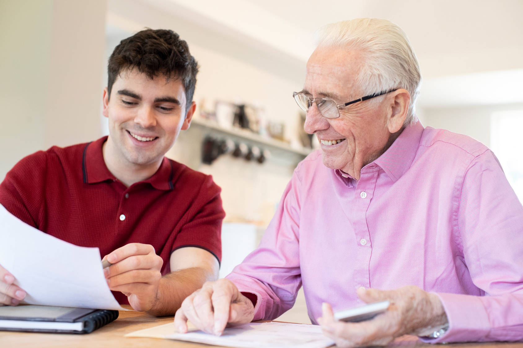 Young Man Helping Senior Neighbor With Paperwork At Home